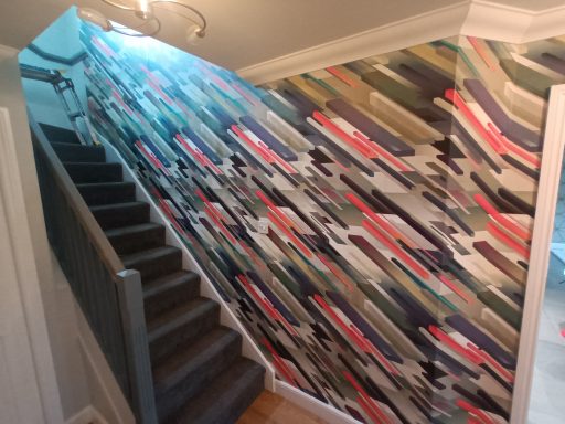 Wall papering the staircase wall in Stirlingshire Staircase with a colourful, abstract wall mural and a chandelier above.