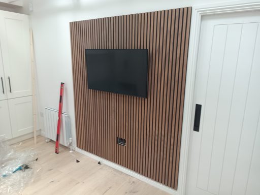 Media wall set up and wall mounted TV Media wall with wooden panelling, mounted TV, and white door in a modern interior space.