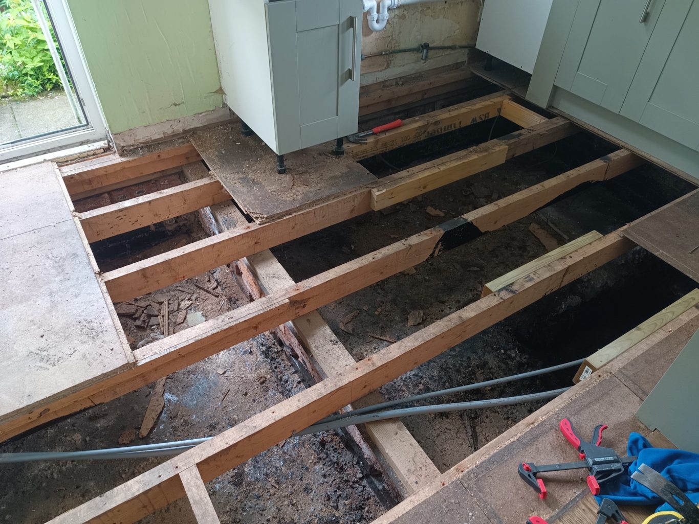 laying new flooring, replacing rotten frame Exposed wooden floor with gaps and exposed beams, showing plumbing underneath. Removed flooring completely to fix rotten frame.