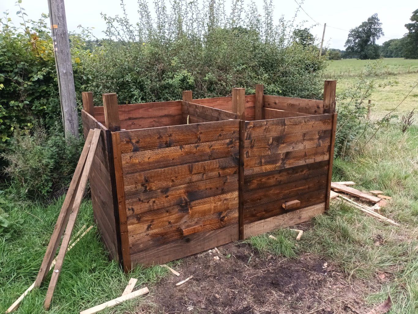 Made a custom compost bin from scratch Wooden compost bin made from rustic planks, set in a grassy outdoor area.